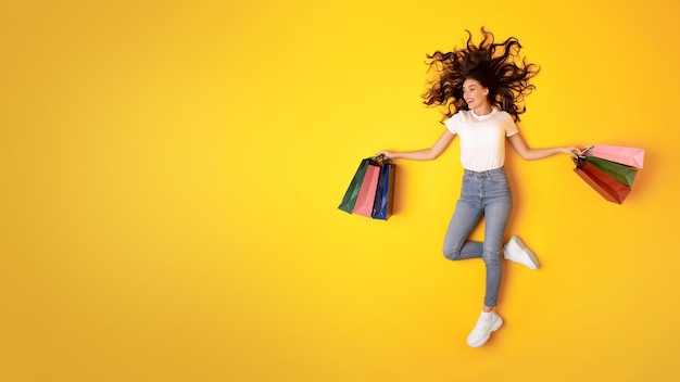 Una compradora feliz posando con bolsas de compras sobre un fondo amarillo