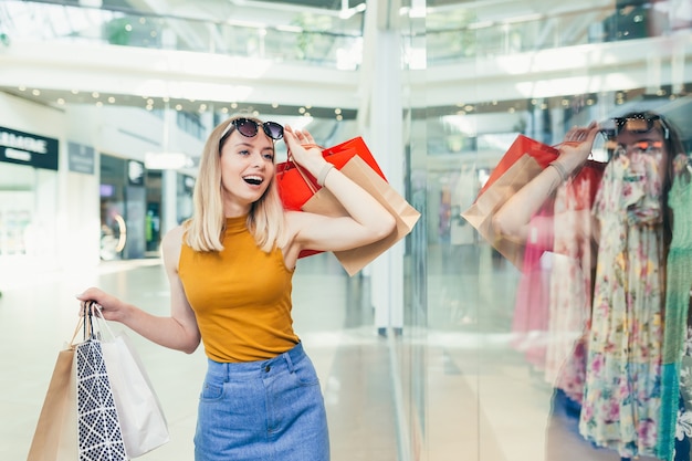 Compradora loira olhando para a vitrine com roupas, procurando com entusiasmo por promoções e descontos