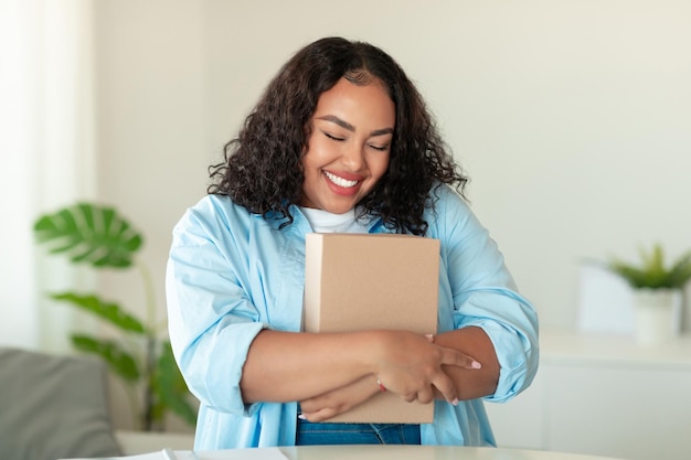 Foto compradora negra feliz abraçando caixa de papelão em casa