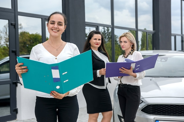 Compradores que miran contrato de compra de coche cerca de coche nuevo