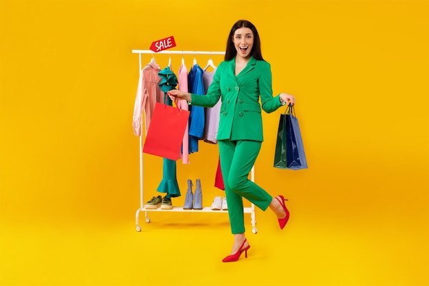 Comprando ropa nueva a la venta señora emocionada sosteniendo coloridas bolsas de compras de pie cerca del riel de ropa
