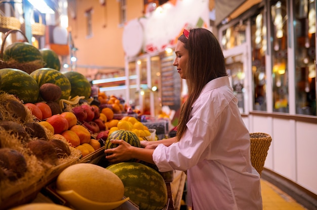 Comprando sandías. Una mujer joven eligiendo una sandía en una tienda de frutas de la calle