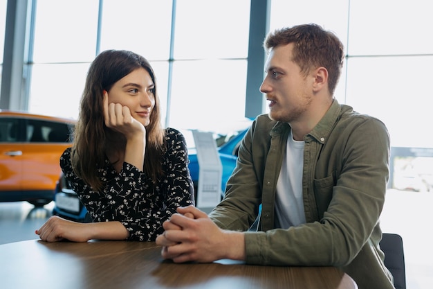 Foto comprar un auto familiar nuevo una pareja joven está sentada en una mesa en un concesionario