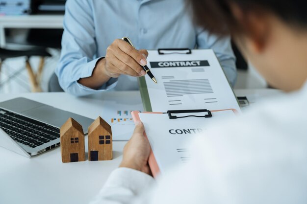 Comprar una casa o un trato de seguros un agente de seguros apuntando con un bolígrafo a aquellos interesados en alquilar una casa un contrato firmando un acuerdo de compra de vivienda en la oficina