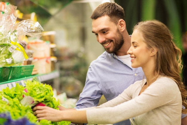 compras, comida, venta, consumismo y concepto de personas - pareja feliz comprando lechuga en la tienda de comestibles o el supermercado