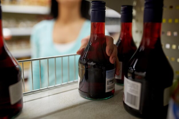 compras, consumismo e conceito de pessoas - mulher pegando uma garrafa de vinagre ou xarope da prateleira do supermercado