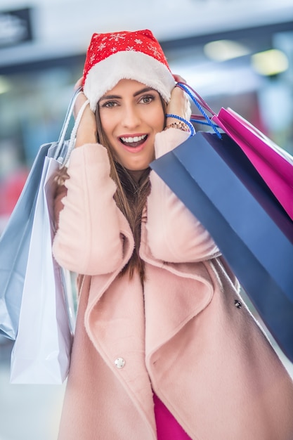 Compras de Natal. Garota atraente feliz com cartão de crédito e sacolas de compras com chapéu de Papai Noel.