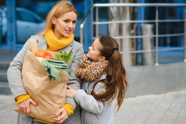 Compras em família. mãe e filha estão segurando uma sacola de compras de supermercado com legumes.