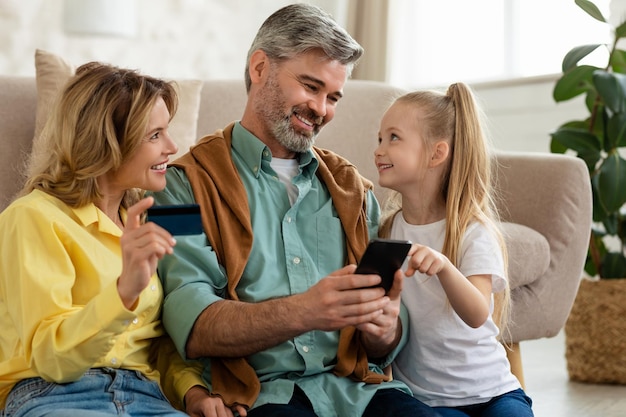 Foto compras em família pagando on-line usando telefone e cartão de crédito interno