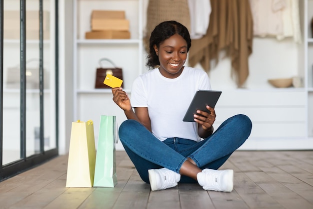 Compras femeninas negras con tarjeta de crédito y tableta en casa