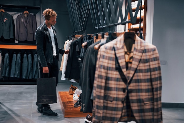 Compras de fin de semana Chico joven en una tienda moderna con ropa nueva Ropa elegante y cara para hombres