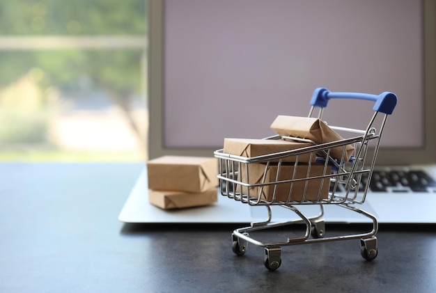 Compras por Internet Carro pequeño con cajas cerca de una computadora portátil moderna en la mesa espacio interior para texto