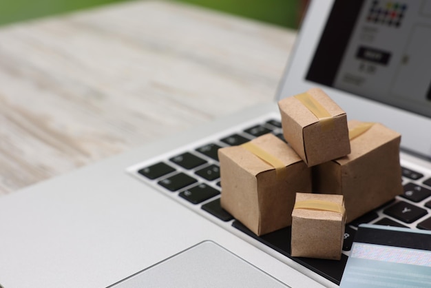 Compras por Internet Pequeñas cajas de cartón tarjeta de crédito y portátil en mesa de madera ligera primer plano Espacio para texto