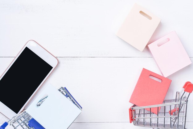 Compras en línea abstractas concepto de pago móvil elemento de diseño carrito colorido y bolsas de papel sobre fondo de mesa de madera blanca vista superior plana