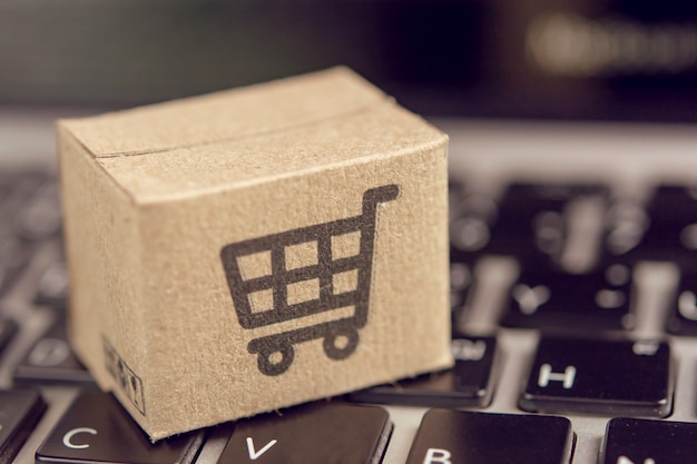 Compras en línea: cajas de cartón o paquetes con el logotipo de un carrito de compras en el teclado de una computadora portátil. Servicio de compras en la web en línea y ofrece servicio a domicilio.