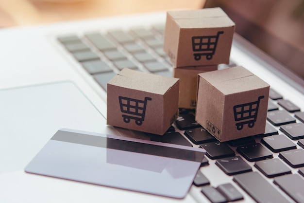 Compras en línea: cajas o paquetes de papel con el logotipo de un carrito de compras y una tarjeta de crédito en el teclado de la computadora portátil. Servicio de compras en la web en línea y ofrece servicio a domicilio.