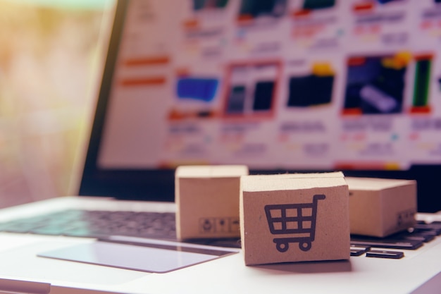 Foto compras en línea: cajas de papel o paquetes con el logotipo de un carrito de compras y una tarjeta de crédito en el teclado de una computadora portátil. servicio de compra en la web online y ofrece entrega a domicilio.