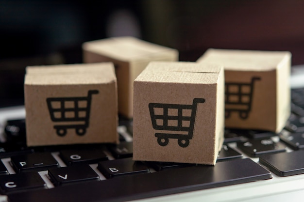 Compras en línea: cajas de papel o paquetes con el logotipo de un carrito de compras en el teclado de una computadora portátil. Servicio de compra en la web online y ofrece entrega a domicilio.