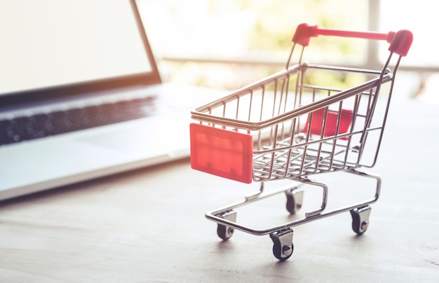 Compras en línea con carrito y computadora portátil.