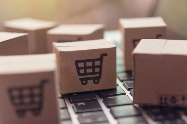 Compras en línea - cartones de papel o paquetes con un logotipo de carrito de compras en un teclado de portátil