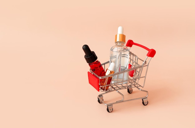 Compras en línea concepto minimalista pequeño carrito con botellas de cosméticos suero de aceite esencial