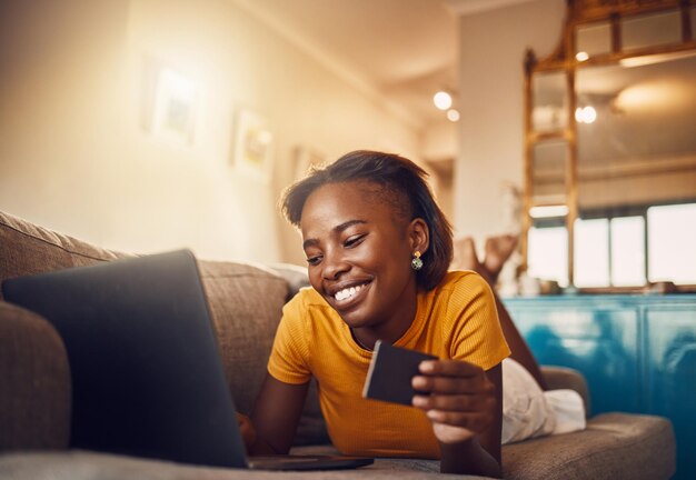 Compras en línea joven mujer africana feliz y sonriente con crédito bancario o tarjeta de regalo Mujer étnica cómoda y alegre emocionada escribiendo en una computadora portátil buscando navegando y comprando regalos desde casa