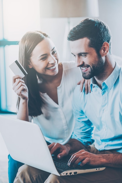 Compras en línea juntos. Hermosa joven pareja amorosa de compras en línea juntos mientras mujer sosteniendo una tarjeta de crédito y sonriendo