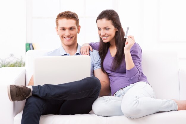 Compras en línea juntos. Hermosa joven pareja amorosa de compras en línea mientras está sentado en el sofá juntos
