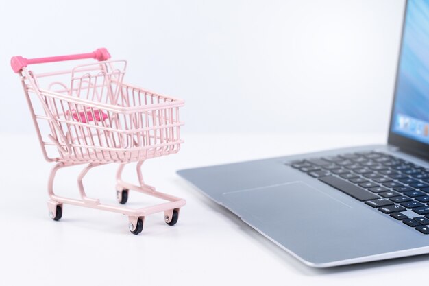 Foto las compras en línea. mini carro de carro de la tienda rosa vacío sobre una computadora portátil sobre fondo blanco de mesa, concepto de compra en casa, cerrar