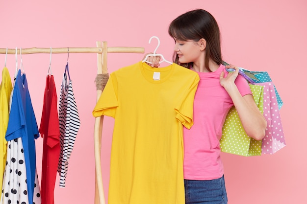 Las compras en línea. La mujer asiática joven con los bolsos de compras intenta en la ropa colorida de la moda en la tienda.