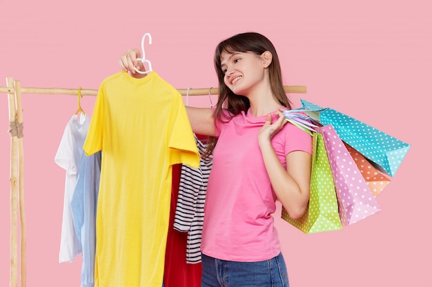 Las compras en línea. La mujer asiática joven con los bolsos de compras intenta en la ropa colorida de la moda en la tienda.