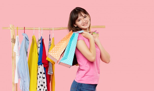 Las compras en línea. La mujer asiática joven con los bolsos de compras intenta en la ropa colorida de la moda en la tienda.