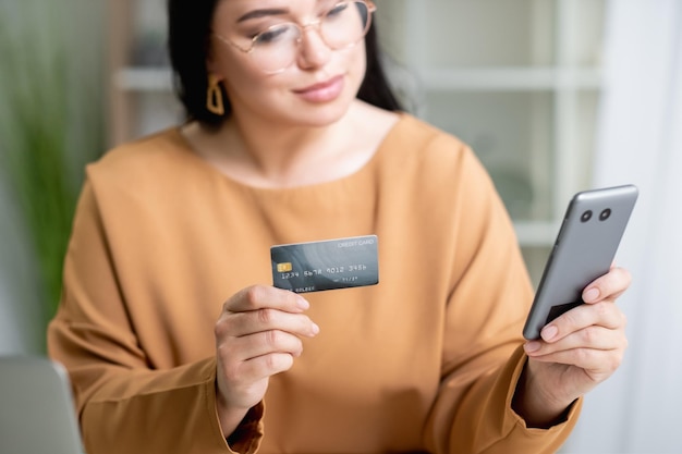 Compras en línea Mujer elegante Pago bancario Transacción rápida Servicio móvil Dama elegante escribiendo teléfono inteligente móvil con tarjeta de crédito interior de la sala de luz