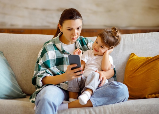 Foto compras en línea niña linda y su madre usando teléfono inteligente en casa