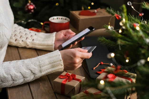 Compras en línea durante las vacaciones Una mujer usa un teléfono y una tarjeta de crédito pide regalos de Navidad