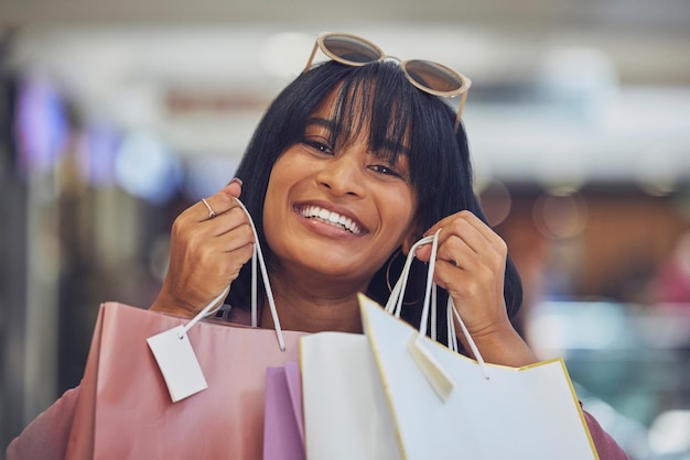 Compras minoristas y retrato de una mujer negra en un centro comercial con bolsas de compras y una sonrisa en la cara Estilo de vida lujoso del cliente y mujer feliz después de comprar ropa, cosméticos y productos en la tienda