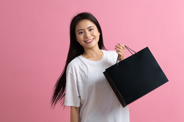 Compras mujer feliz asiática sosteniendo bolsas de compras sobre fondo rosa