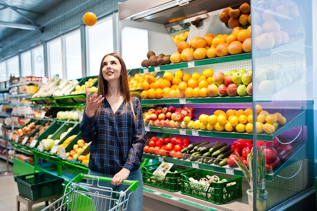 Compras mujer mirando los estantes en el supermercado con carrito de compras Retrato de una niña en una tienda de mercado en la sección de frutas y verduras