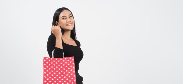 Compras de mujer sexy. Hermosa chica vestida de negro sosteniendo bolsas rojas aisladas sobre blanco