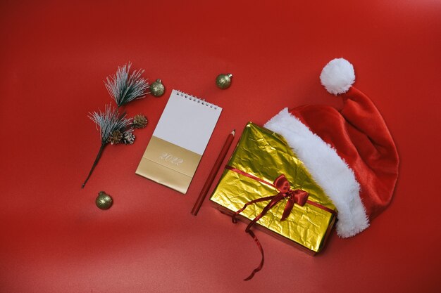 Compras de Navidad. Lista de compras y regalos para el nuevo año. Sombrero de Papá Noel se encuentra en una caja de oro sobre un fondo rojo.