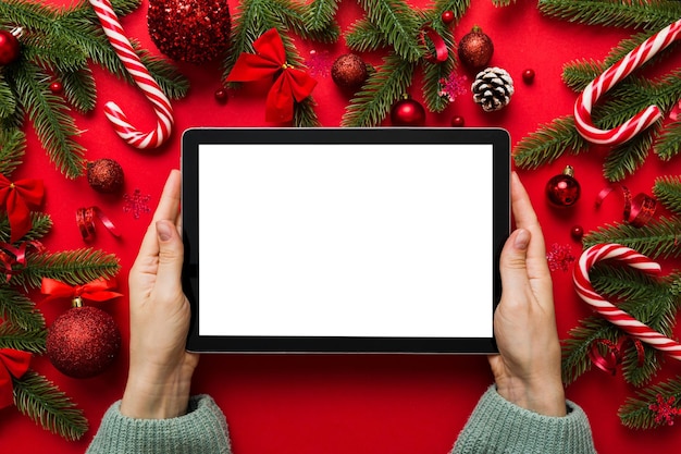 Compras navideñas en línea desde casa manos femeninas sosteniendo tablet pc con pantalla blanca en blanco vista superior mano de mujer sosteniendo tableta con pantalla en blanco árbol de Navidad y regalos en el fondo