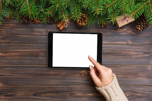 Compras navideñas en línea. Pantalla táctil de mano femenina de tableta, vista superior en bakground de madera, copyspace. Fondo de ventas de vacaciones de invierno