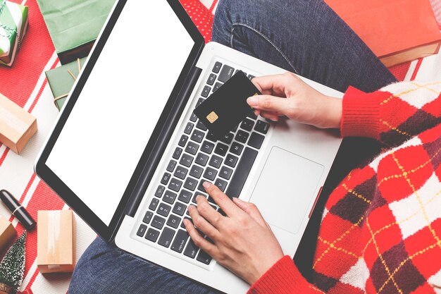 Compras navideñas online. Compradora femenina con laptop, prepárate para la víspera de Navidad, sentada entre cajas y paquetes de regalos. Rebajas de vacaciones de invierno