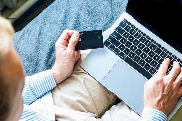 compras on-line com cartão de crédito, um homem se senta em uma cama em um computador, compra nas mãos