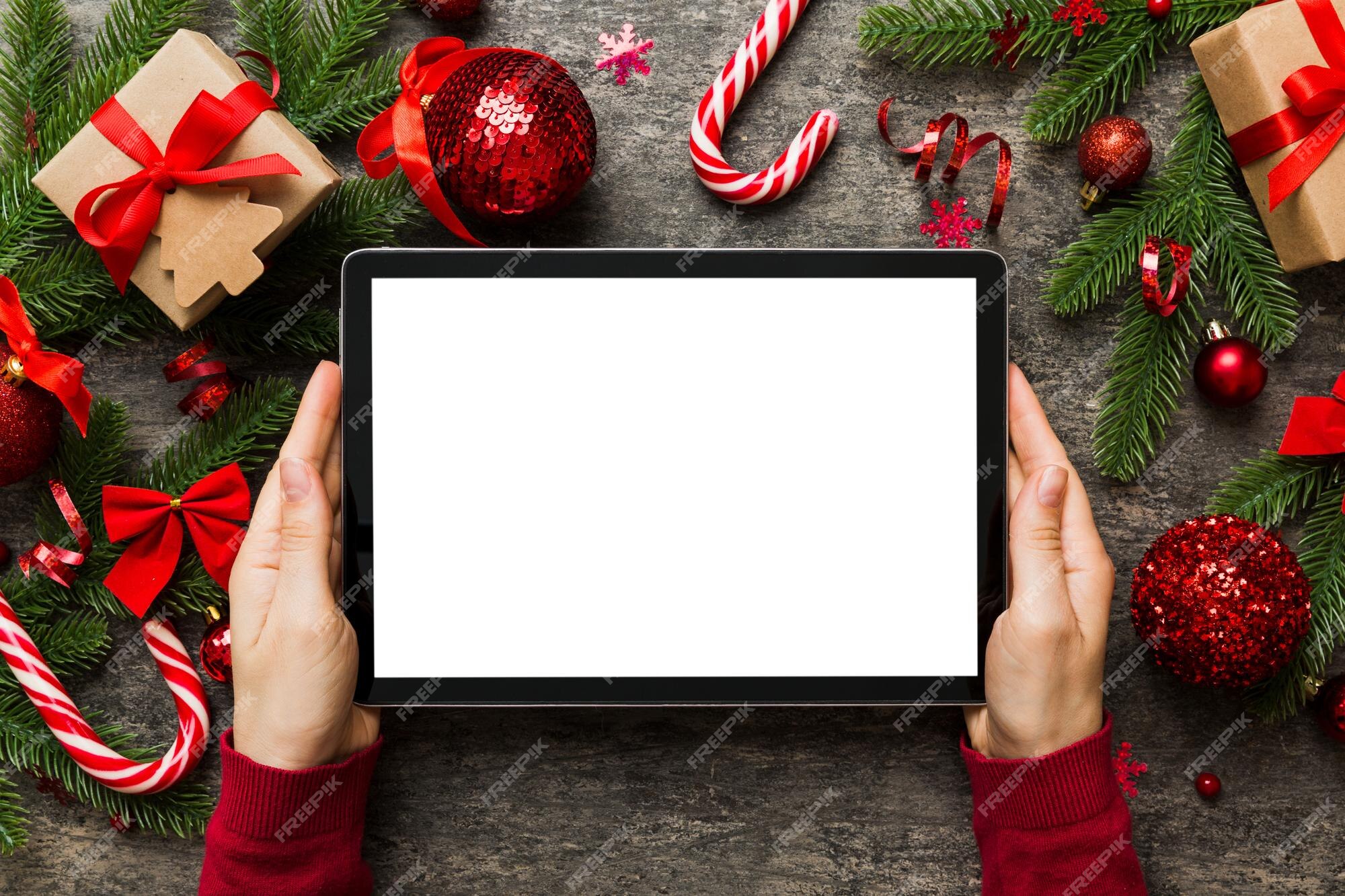 Compras on-line de natal em casa mãos femininas segurando tablet pc com tela branca em branco vista superior mão de mulher segurando tablet com tela em branco árvore de natal e presentes Compras on-line de natal em casa mãos femininas segurando tablet pc com tela branca em branco vista superior mão de mulher segurando tablet com tela em branco árvore de natal e presentes