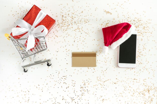 Compras online de Natal. Mini carrinho de compras, celular, cartão de crédito e caixa de presente, vista de cima