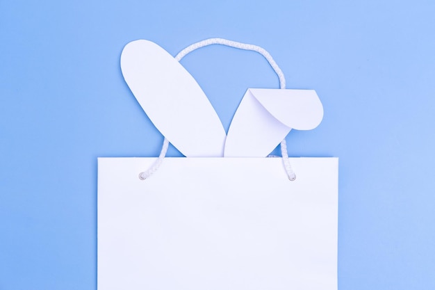 Foto compras para a páscoa saco de compras de papel branco com orelhas de coelho brancas sobre fundo azul conceito presentes de páscoa