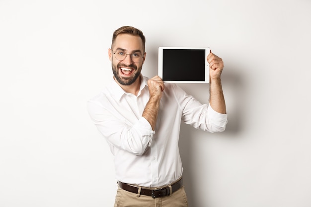 Compras y tecnología. Hombre guapo mostrando la pantalla de la tableta digital, con gafas con camisa de cuello blanco, fondo de estudio.