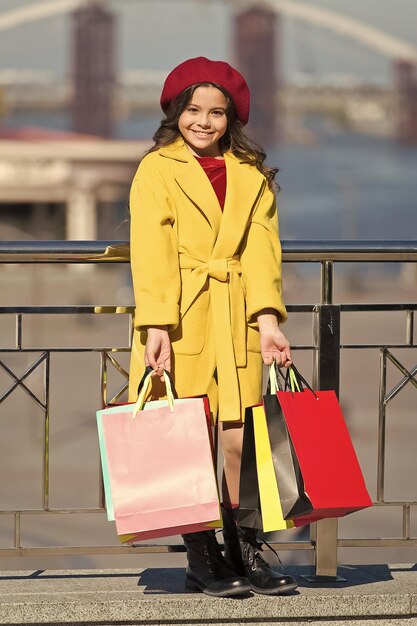 Compre ropa y accesorios para la temporada de primavera Compras de niños pequeños Niño con estilo sostiene un montón de bolsas de compras Chica linda dama abrigo y boina llevan bolsas de compras Concepto de compras de primavera