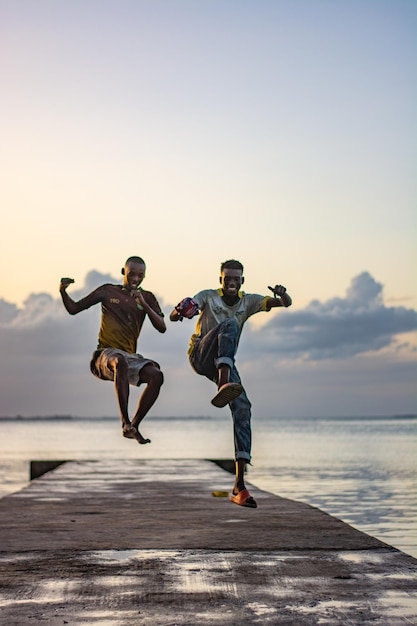 Comprimento completo de dois homens pulando na praia contra o céu claro durante o pôr do sol